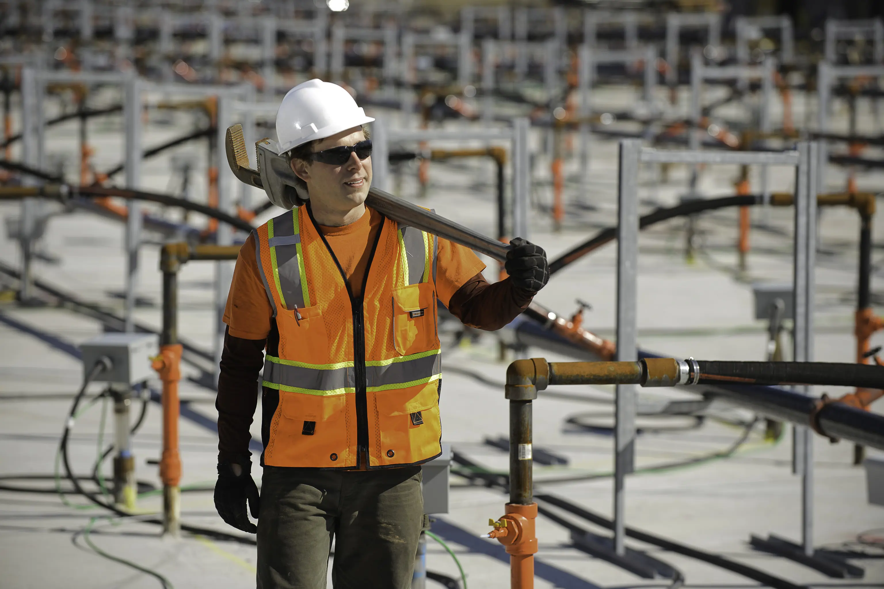 a worker standing in a well field with a wrench over his shoulder